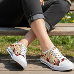 A woman wearing colorful, patterned sneakers and black rolled-up jeans sits on a wooden bench outdoors, legs crossed, with green grass and flowers in the background.