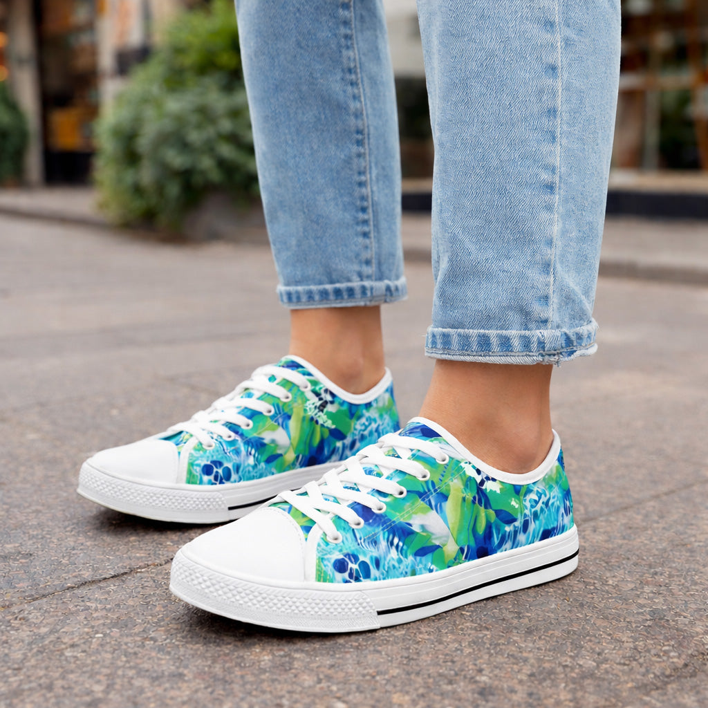 Womanwearing light blue jeans and colorful sneakers with a blue, green, and white floral pattern stands on a city sidewalk. The focus is on the shoes and lower legs.