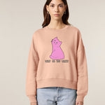 woman wearing a beige sweatshirt with a pink cat graphic and text on a plain background