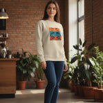 A woman stands indoors by potted plants, wearing a beige sweatshirt with colorful eye illustrations on the front. She has long brown hair and is dressed in blue jeans, with a brick wall and large windows in the background.