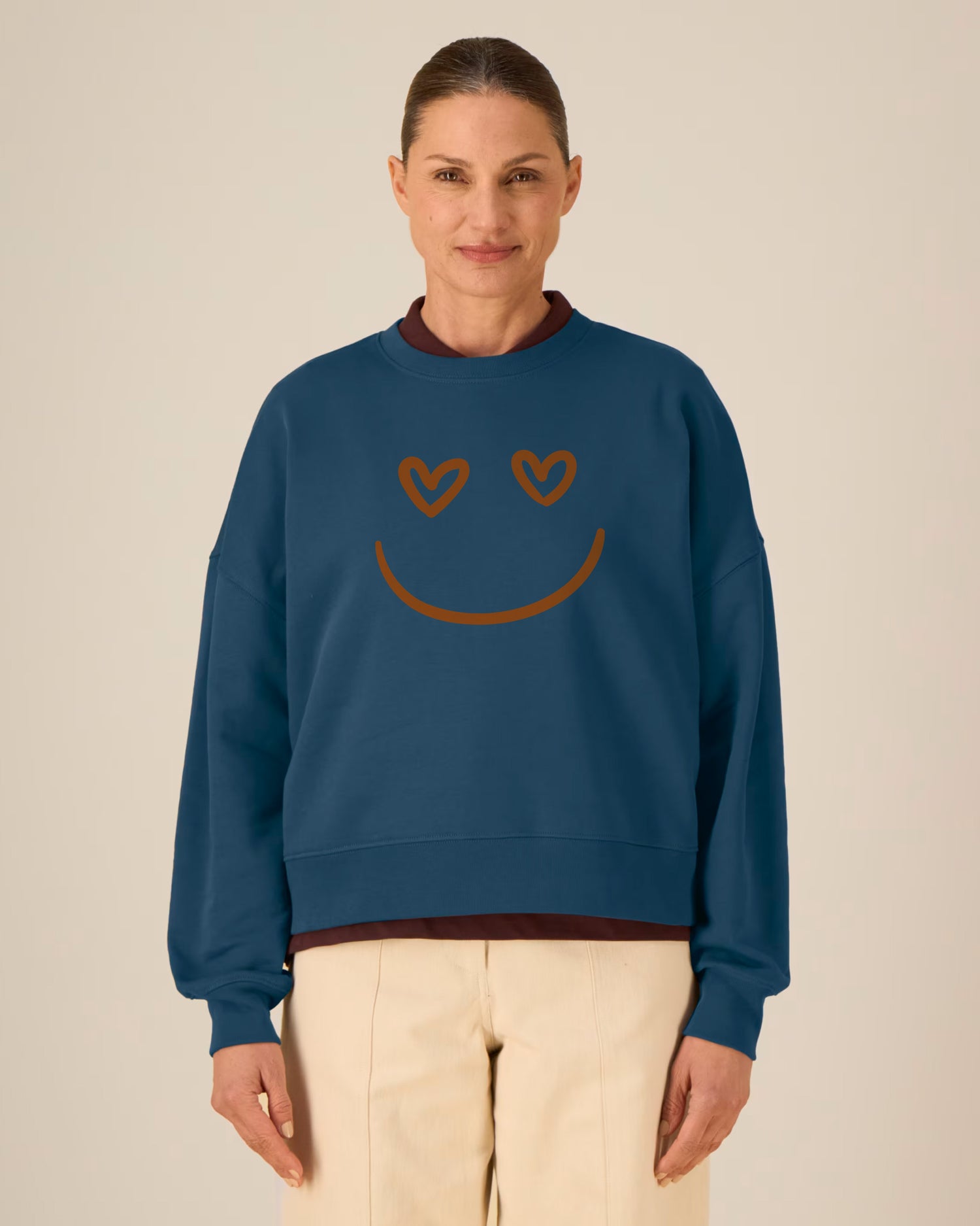 Woman wearing a blue sweatshirt with a smiley face design on a beige background
