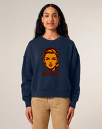 A woman with long dark hair wears a navy blue sweatshirt featuring a stylized graphic of a woman's face and the words "I'M FEARLESS" in bold red letters. She is standing and smiling slightly.