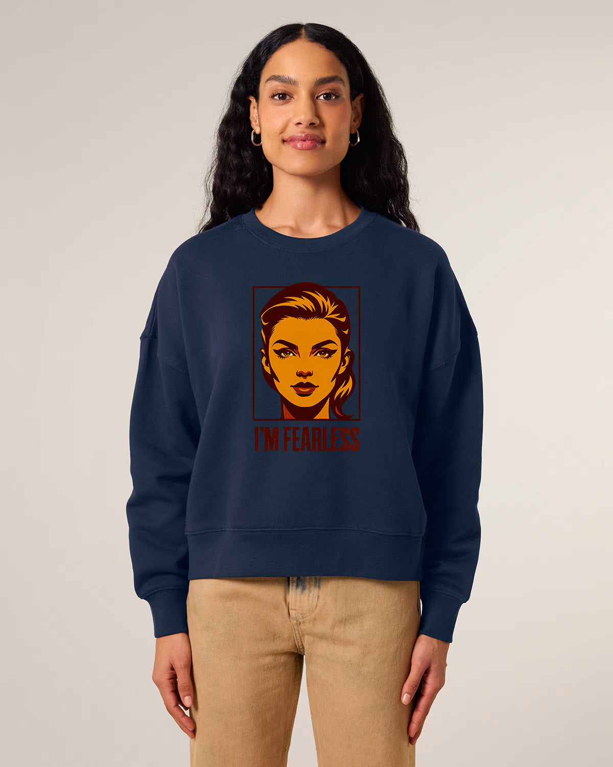 A woman with long dark hair wears a navy blue sweatshirt featuring a stylized graphic of a woman's face and the words "I'M FEARLESS" in bold red letters. She is standing and smiling slightly.