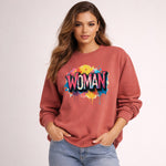 Woman wearing a red sweatshirt with 'WOMAN' in colorful letters on a light pink background