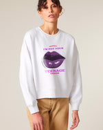 A woman wearing a white sweatshirt with a large graphic of purple lips and the text "SORRY I'M NOT YOUR TEENAGE DREAM" in pink and purple letters, paired with tan pants.