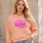 Woman wearing a peach sweatshirt with a graphic design in front of a neutral background