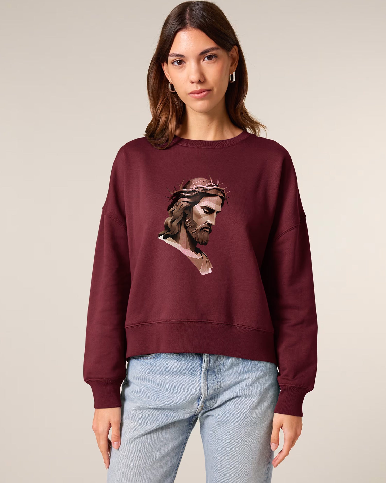 A woman wearing a maroon sweatshirt with a graphic illustration of Jesus with a crown of thorns on the front, standing against a plain light background.