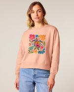 Woman wearing a pink sweatshirt with a colorful floral design on a plain background