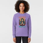 A woman wearing a lavender sweatshirt with an illustration of a praying figure surrounded by flowers and the text "Pray More Worry Less" stands facing forward, smiling slightly against a plain background.