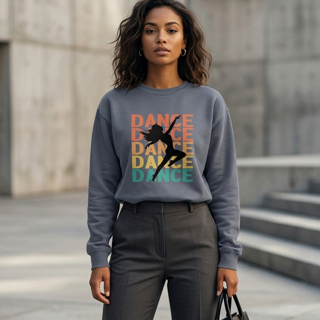 A woman stands outdoors wearing a gray sweatshirt with the word "DANCE" in colorful letters and a silhouette of a dancer. She has wavy hair, gray trousers, and holds a black bag. The background features concrete walls and steps.