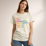 A woman wearing a light-colored T-shirt with the text "Girls just wanna have fundamental human rights" printed in multicolored letters, standing against a neutral background.
