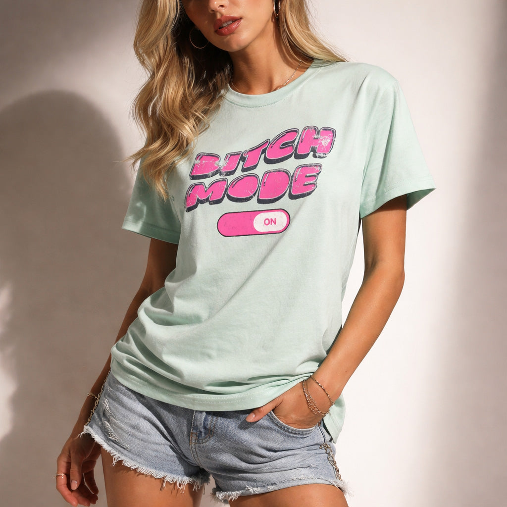 woman wearing a light green t-shirt with pink text and denim shorts on a plain background