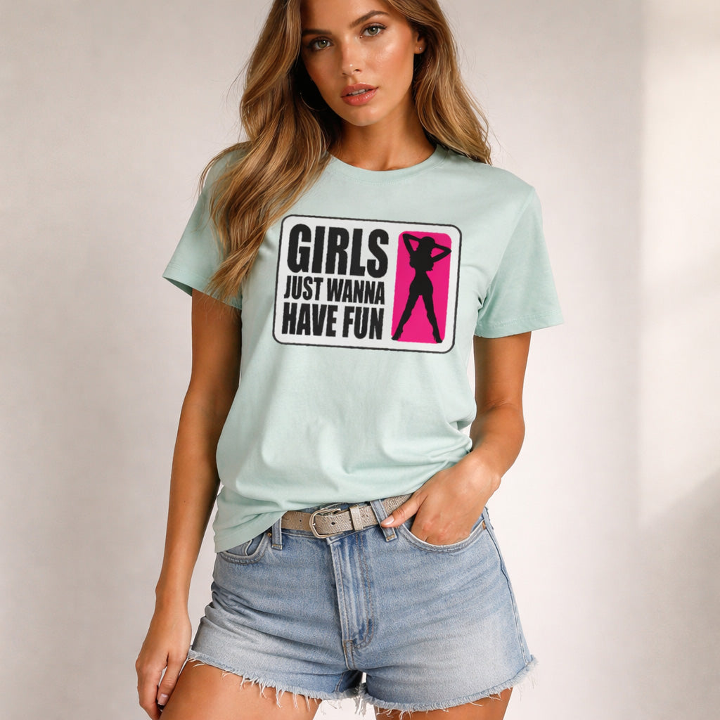 A woman wearing a light blue T-shirt with the text "Girls Just Wanna Have Fun" and a pink silhouette of a woman, paired with light denim shorts, standing against a plain background.