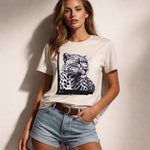 Woman wearing a white t-shirt with a leopard graphic and denim shorts against a neutral background