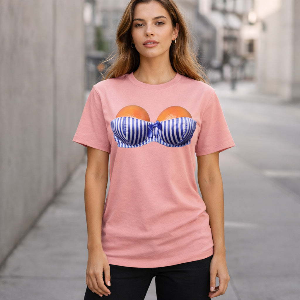 A woman stands outdoors wearing a pink t-shirt with a graphic of two peaches inside a blue and white striped bra printed on the front. She has long hair and a neutral expression.
