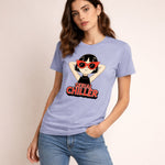 A woman wearing a light purple t-shirt with a cartoon of a girl in red sunglasses and the words "Serial Chiller" printed on it. She stands against a plain light background and looks at the camera.