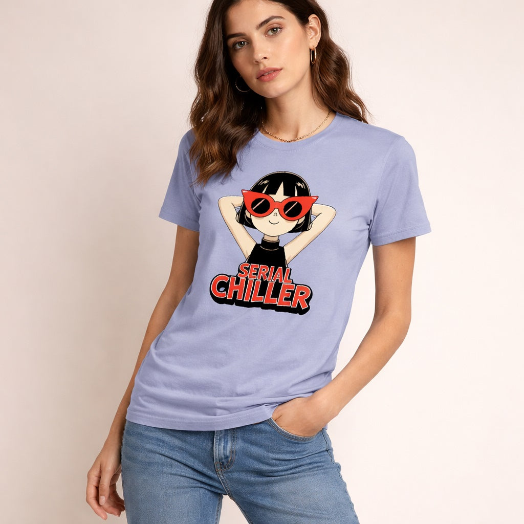 A woman wearing a light purple t-shirt with a cartoon of a girl in red sunglasses and the words "Serial Chiller" printed on it. She stands against a plain light background and looks at the camera.