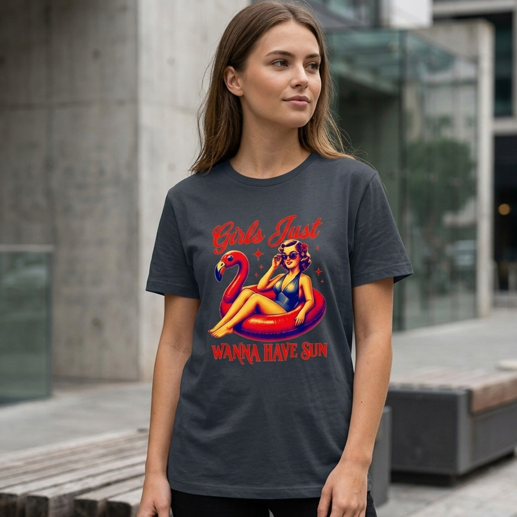 A woman stands outdoors wearing a dark T-shirt featuring a retro illustration of a woman lounging on a pink flamingo float, with the text "Girls Just Wanna Have Sun.