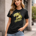 A woman in a black t-shirt with a gold lioness graphic and the words "WILD QUEEN" stands outside on a city street, resting one hand in her jeans pocket.